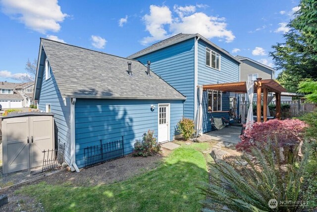 rear view of house with a patio, roof with shingles, a storage shed, and fence
