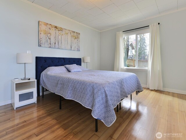 bedroom with baseboards, ornamental molding, and wood finished floors