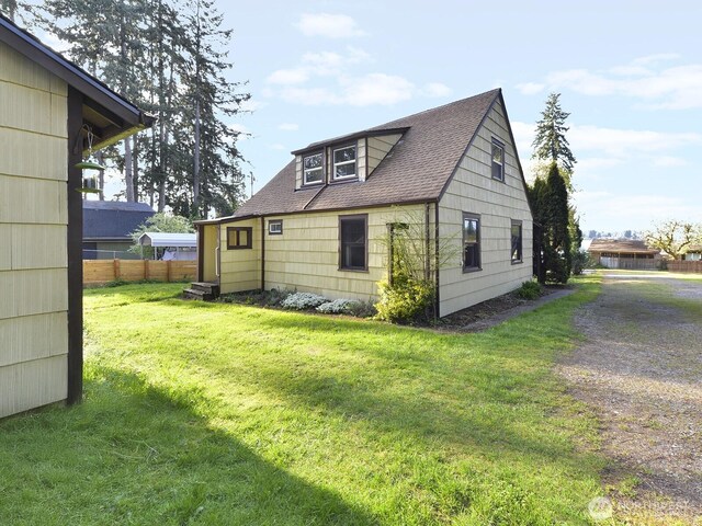 view of property exterior with a lawn, fence, and roof with shingles