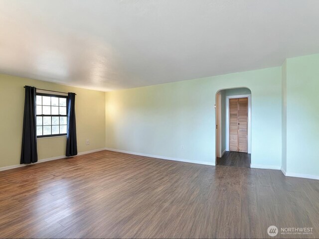 spare room featuring arched walkways, baseboards, and dark wood-type flooring