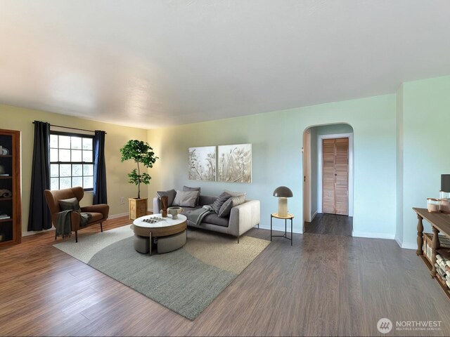 living room with arched walkways, baseboards, and dark wood-type flooring