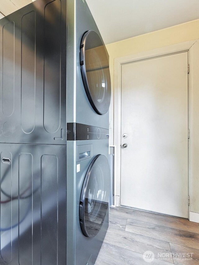laundry room with stacked washer / drying machine, wood finished floors, and laundry area