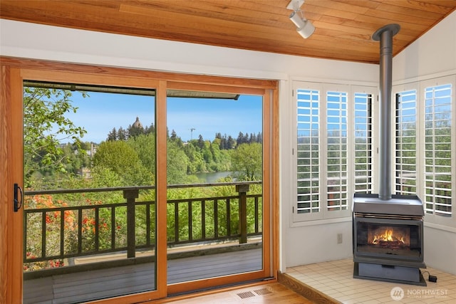 doorway to outside featuring visible vents, a wood stove, a water view, and wooden ceiling