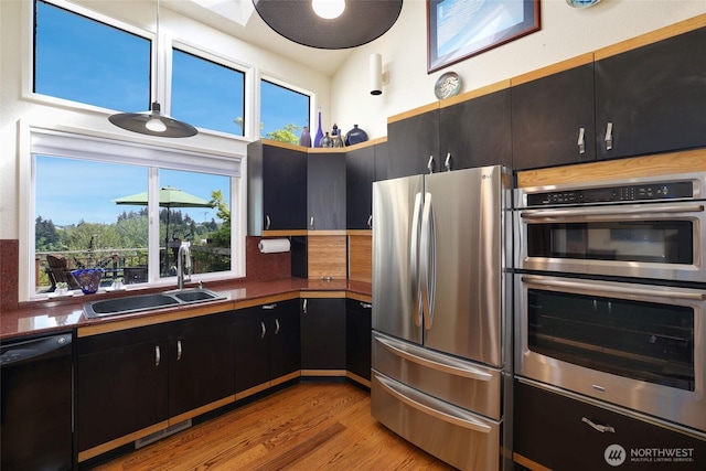 kitchen with appliances with stainless steel finishes, a sink, light wood finished floors, dark cabinetry, and decorative backsplash