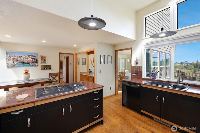 kitchen featuring stainless steel gas cooktop, black dishwasher, light wood-type flooring, dark cabinets, and a sink