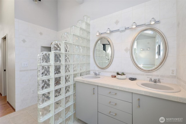 full bath featuring double vanity, a sink, walk in shower, and tile walls