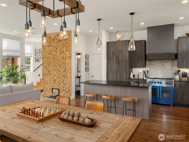 kitchen featuring a kitchen breakfast bar, decorative backsplash, dark countertops, premium range hood, and range with two ovens
