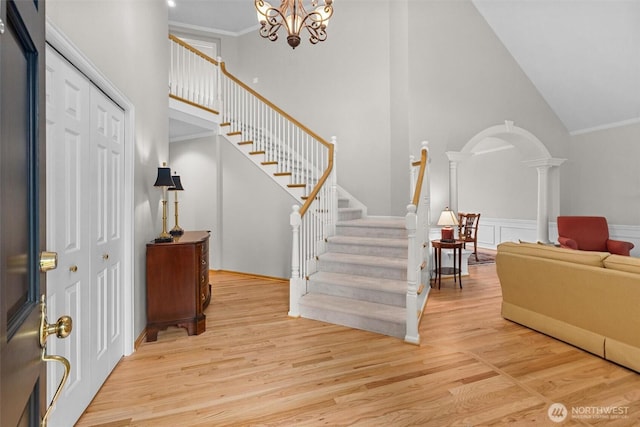entryway featuring arched walkways, high vaulted ceiling, decorative columns, wood finished floors, and stairway