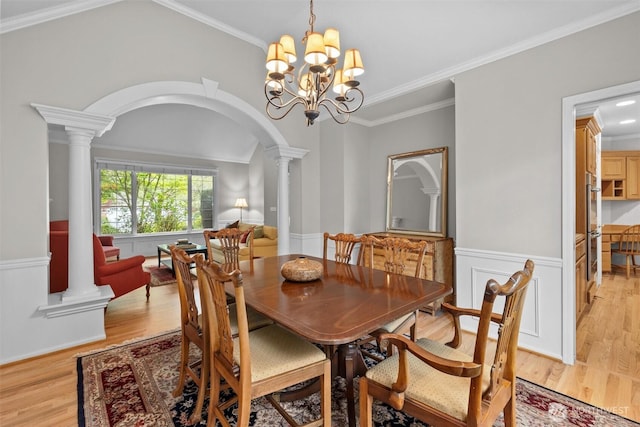 dining room with a notable chandelier, light wood-style floors, arched walkways, a wainscoted wall, and decorative columns