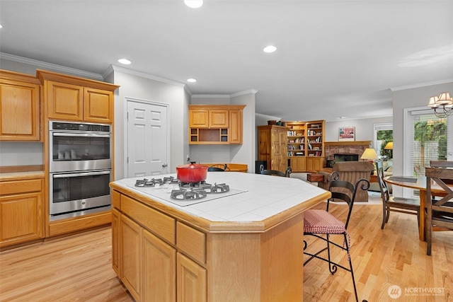 kitchen with a kitchen island, a brick fireplace, double oven, white gas cooktop, and tile counters