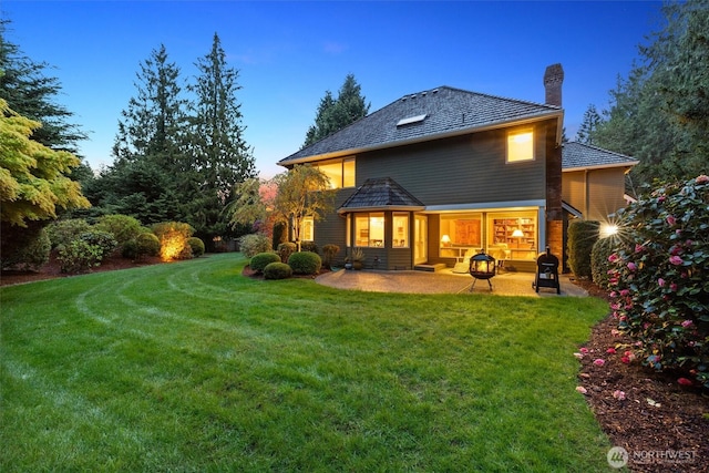 back of house at dusk featuring a patio area, a yard, and a chimney