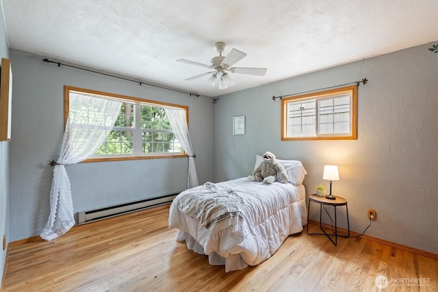 1302 Spruce St, Longview, WA 98632 - bedroom featuring a baseboard radiator, light wood finished floors, baseboards, a ceiling fan, and a textured wall