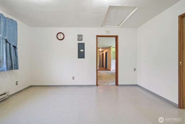 unfurnished room with baseboards, attic access, and electric panel