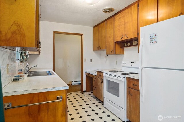 kitchen featuring brown cabinets, a sink, light countertops, a baseboard heating unit, and white appliances