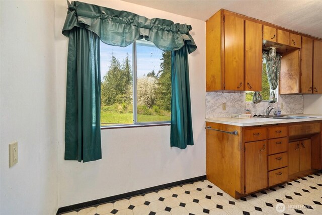 kitchen featuring a sink, brown cabinets, light countertops, baseboards, and light floors