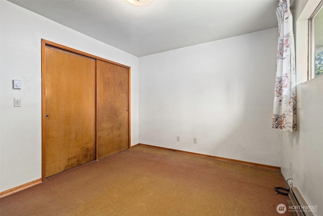 unfurnished bedroom with a baseboard radiator, baseboards, carpet flooring, and a closet