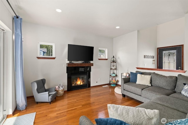living area featuring a glass covered fireplace, recessed lighting, baseboards, and light wood-type flooring