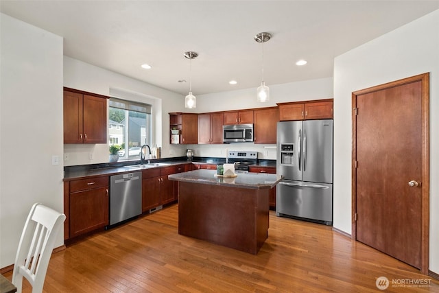 kitchen featuring hardwood / wood-style floors, stainless steel appliances, dark countertops, a sink, and a center island