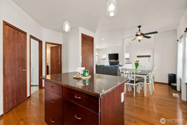 kitchen with light wood-type flooring, a center island, a ceiling fan, visible vents, and decorative light fixtures