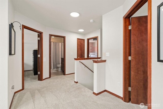 hall with baseboards, light carpet, and an upstairs landing