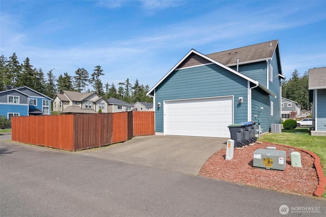 view of property exterior featuring driveway, cooling unit, a residential view, an attached garage, and fence