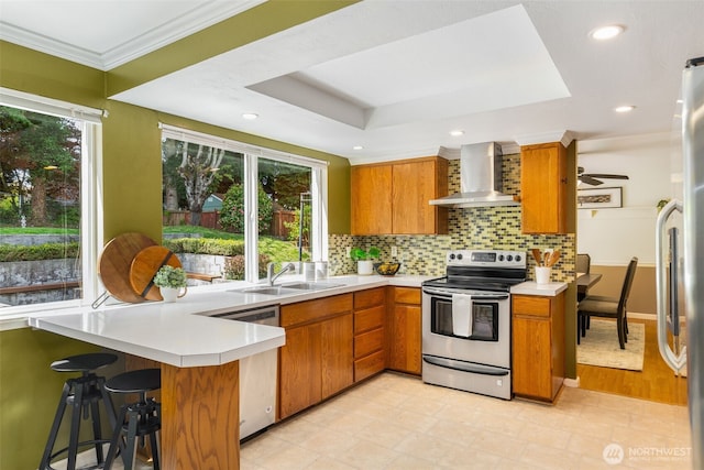 kitchen with a sink, wall chimney exhaust hood, appliances with stainless steel finishes, and brown cabinets