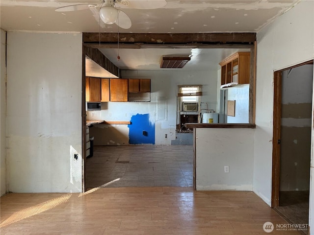 kitchen featuring beamed ceiling, a ceiling fan, wood finished floors, and brown cabinetry