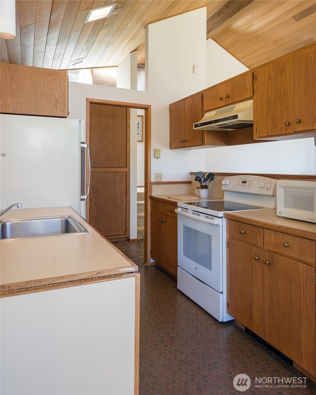 kitchen with vaulted ceiling with beams, white appliances, brown cabinetry, under cabinet range hood, and a sink