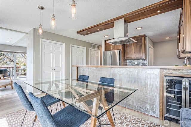 dining space featuring beverage cooler, light wood-style floors, a textured ceiling, and recessed lighting
