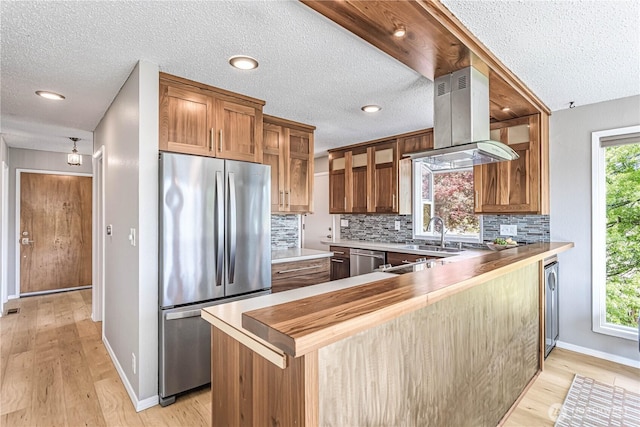 kitchen featuring stainless steel appliances, island range hood, a sink, a textured ceiling, and decorative backsplash