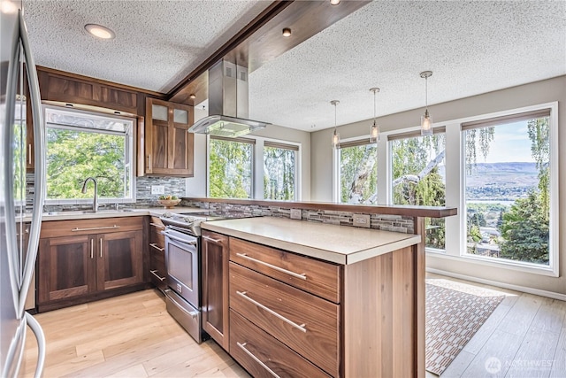 kitchen featuring appliances with stainless steel finishes, a peninsula, island exhaust hood, a textured ceiling, and decorative backsplash