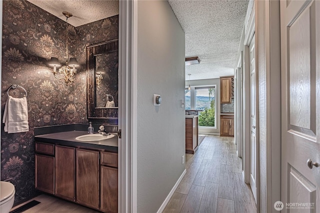 bathroom featuring a textured ceiling, vanity, wood finished floors, baseboards, and toilet