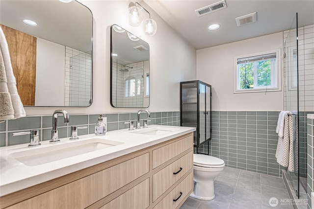 full bath with tile walls, tile patterned floors, toilet, double vanity, and a shower