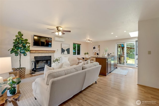 living room with ceiling fan, recessed lighting, a wall mounted AC, a tiled fireplace, and light wood-style flooring