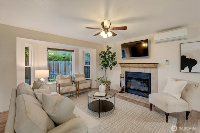 living room with a ceiling fan, a wall unit AC, wood finished floors, and a fireplace