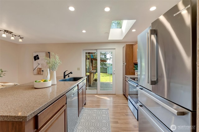 kitchen with brown cabinets, a sink, light wood finished floors, appliances with stainless steel finishes, and a skylight