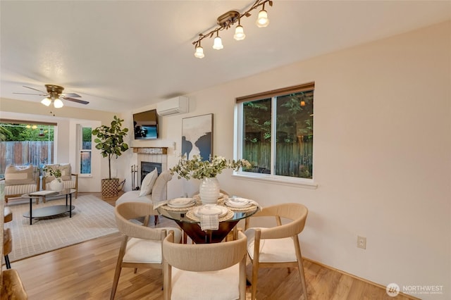 dining area with ceiling fan, a wall unit AC, wood finished floors, and a tile fireplace