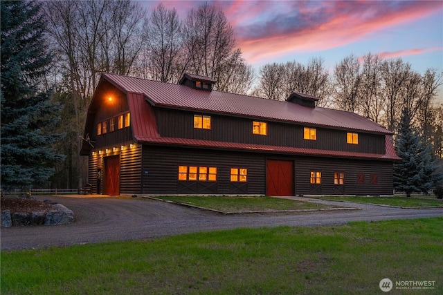 cabin featuring a chimney, a gambrel roof, metal roof, dirt driveway, and a detached garage