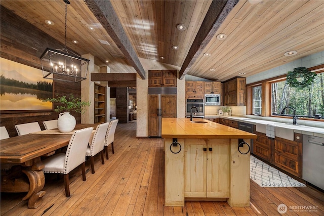 kitchen featuring vaulted ceiling with beams, built in appliances, wooden counters, light wood finished floors, and a notable chandelier