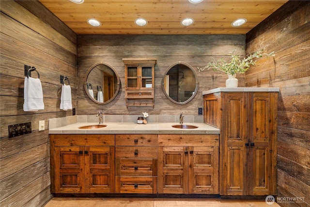 bathroom with wooden walls, recessed lighting, and a sink