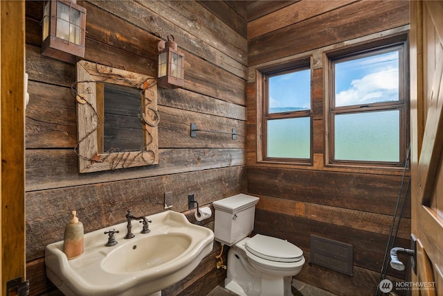 half bath with wooden walls, a sink, toilet, and visible vents