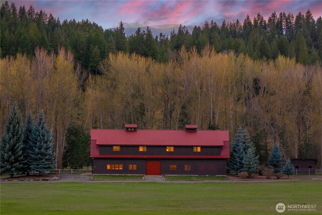view of front of property with a chimney, metal roof, fence, a yard, and a forest view