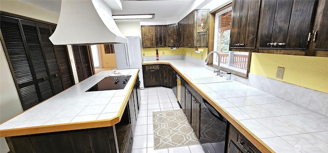 kitchen with black electric stovetop, a sink, premium range hood, dark brown cabinetry, and tile countertops