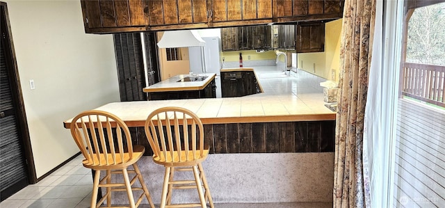 kitchen with light tile patterned floors, custom range hood, tile counters, a sink, and a peninsula