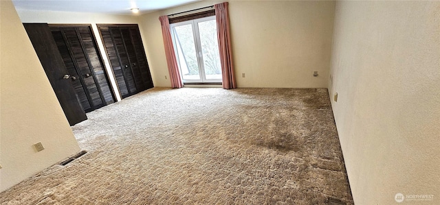 unfurnished bedroom with a textured wall, multiple closets, and carpet floors