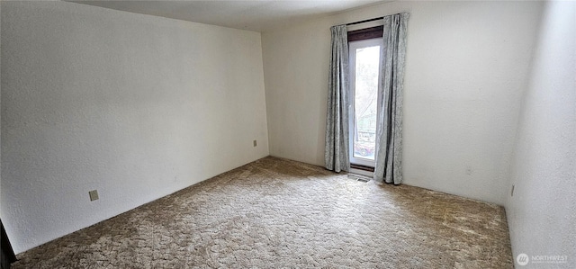 unfurnished room with carpet, visible vents, and a textured wall