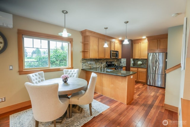 kitchen with decorative backsplash, dark countertops, light wood finished floors, a peninsula, and stainless steel appliances