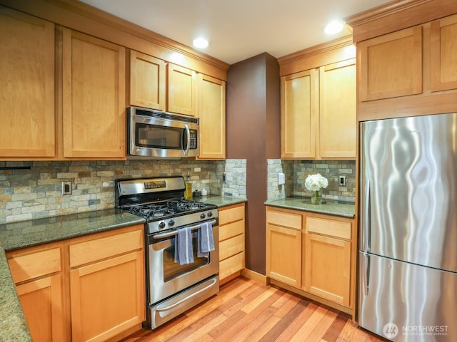 kitchen with dark stone counters, backsplash, appliances with stainless steel finishes, and light wood finished floors
