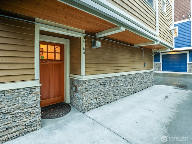 doorway to property featuring an attached garage, driveway, and stone siding
