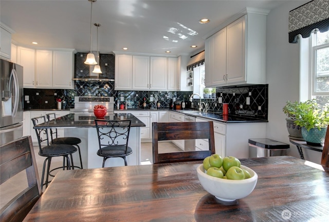 kitchen with stainless steel appliances, decorative backsplash, wall chimney range hood, dark countertops, and white cabinets